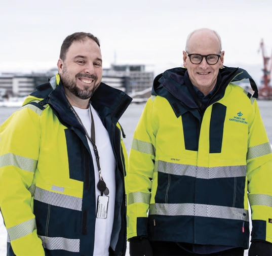 Två personer utomhus i varseljackor. 