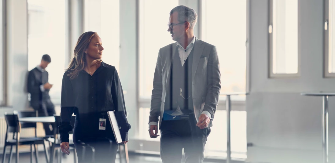 Två personer som går jämte varandra i ett kontorslandskap.