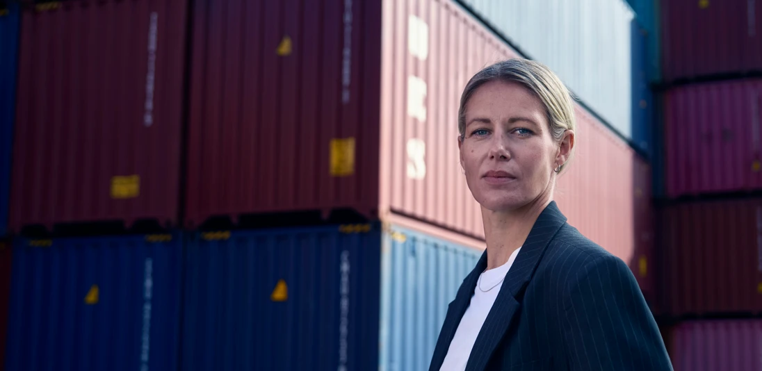 Kvinna som tittar in i kameran med containrar i bakgrunden.